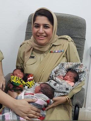 Dr. Hina Urooj in military medical uniform holding three healthy newborn triplets at Hina's Clinic. Best Gynaecologist in Islamabad
