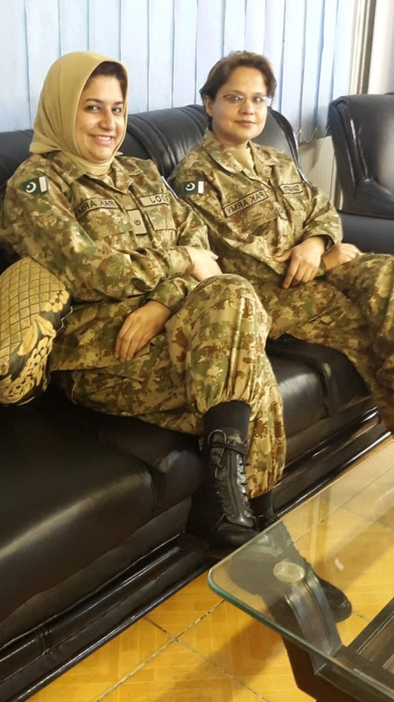 Dr. Urooj Hina in Pakistan Army camouflage uniform sitting on a sofa with a colleague, showcasing female empowerment in the military.