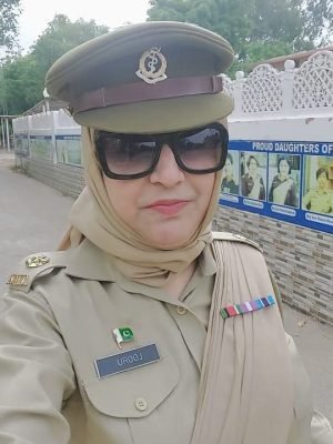 Pakistani female medical officer Ex. Major Dr. Urooj Hina in official AMC uniform with a backdrop of "Proud Daughters of Pakistan" posters.